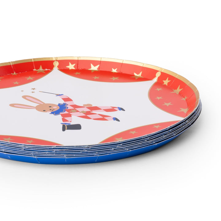 A stack of round paper party plates with a circus theme, featuring a rabbit in a red and white checkered outfit on a white center, red curtains with gold stars, and blue rims.