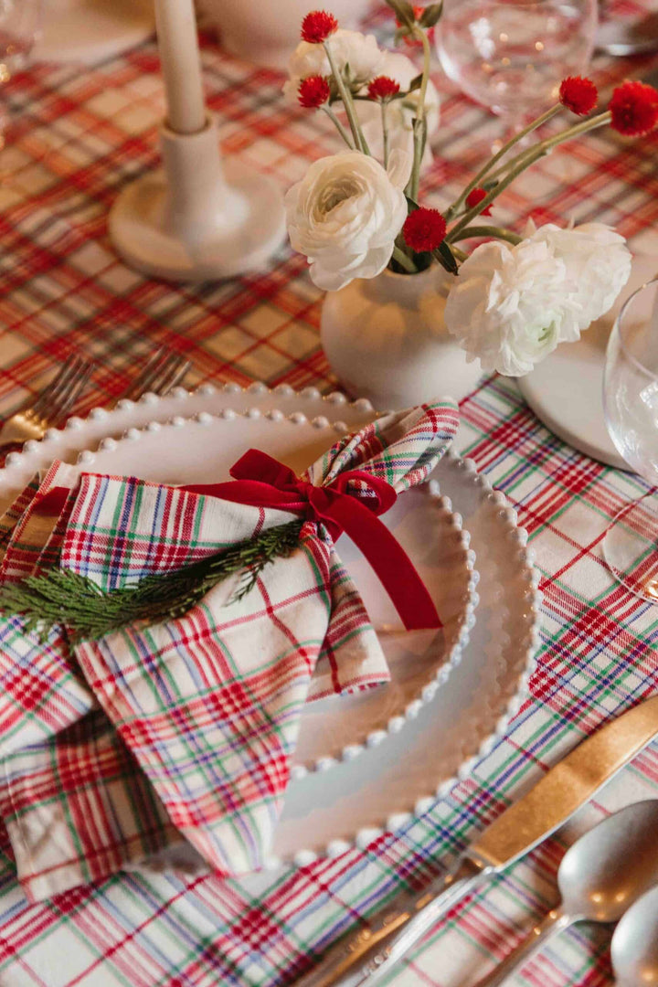 Clara plaid napkin tied with a red ribbon and greenery on a beaded plate at a Christmas table