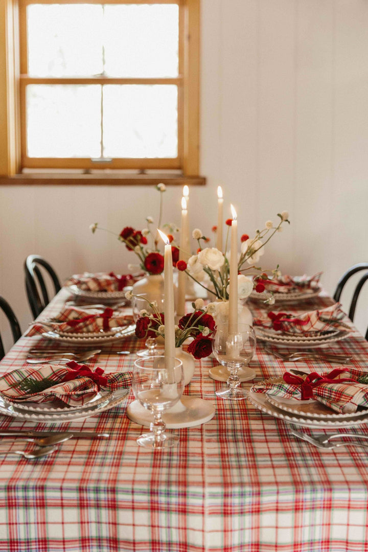 Christmas dining room with a Clara plaid tablecloth beneath a wreath on a white brick wall