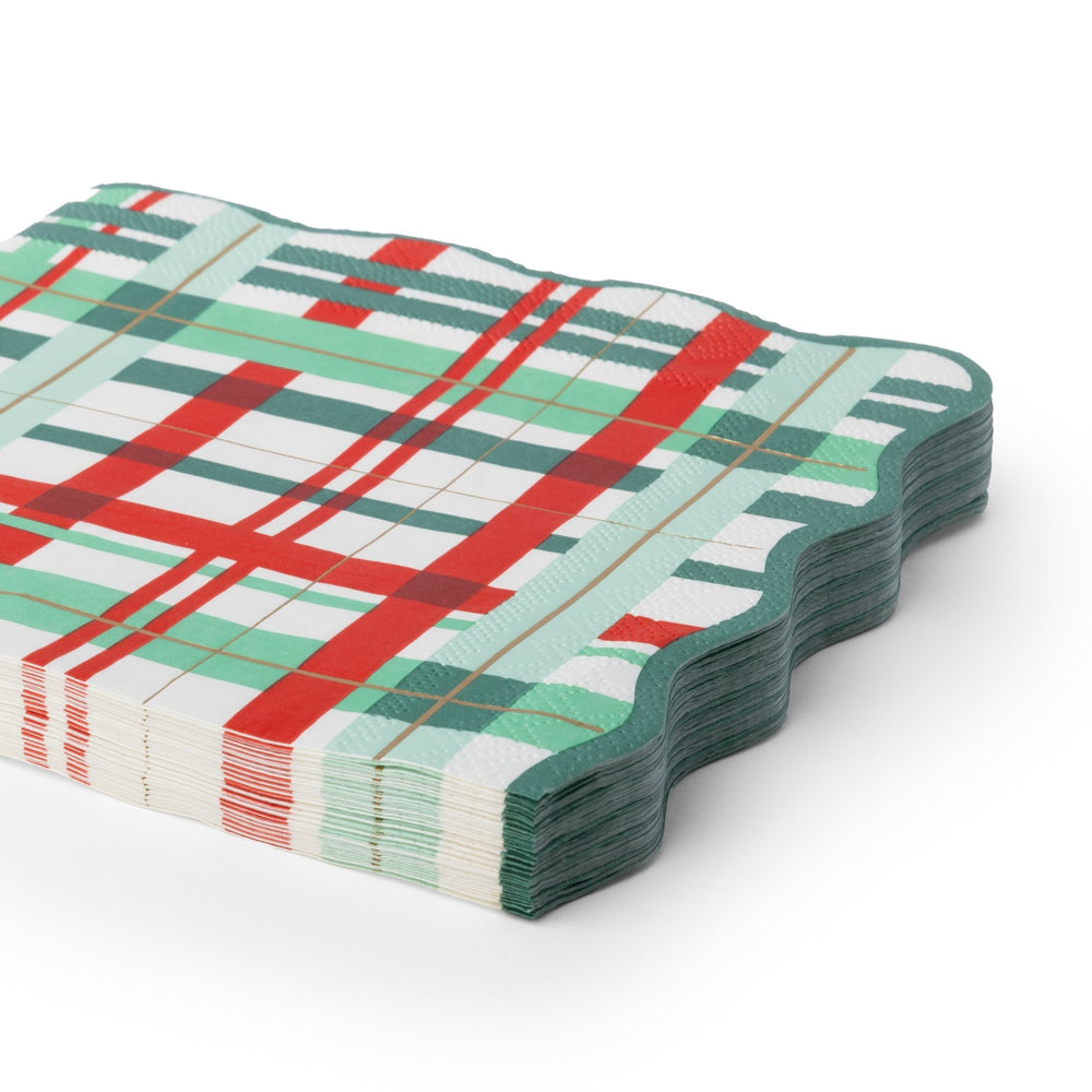 A stack of scalloped-edge paper napkins featuring a festive holiday plaid pattern in red, green, and white with thin gold lines, shown on a clean white background.