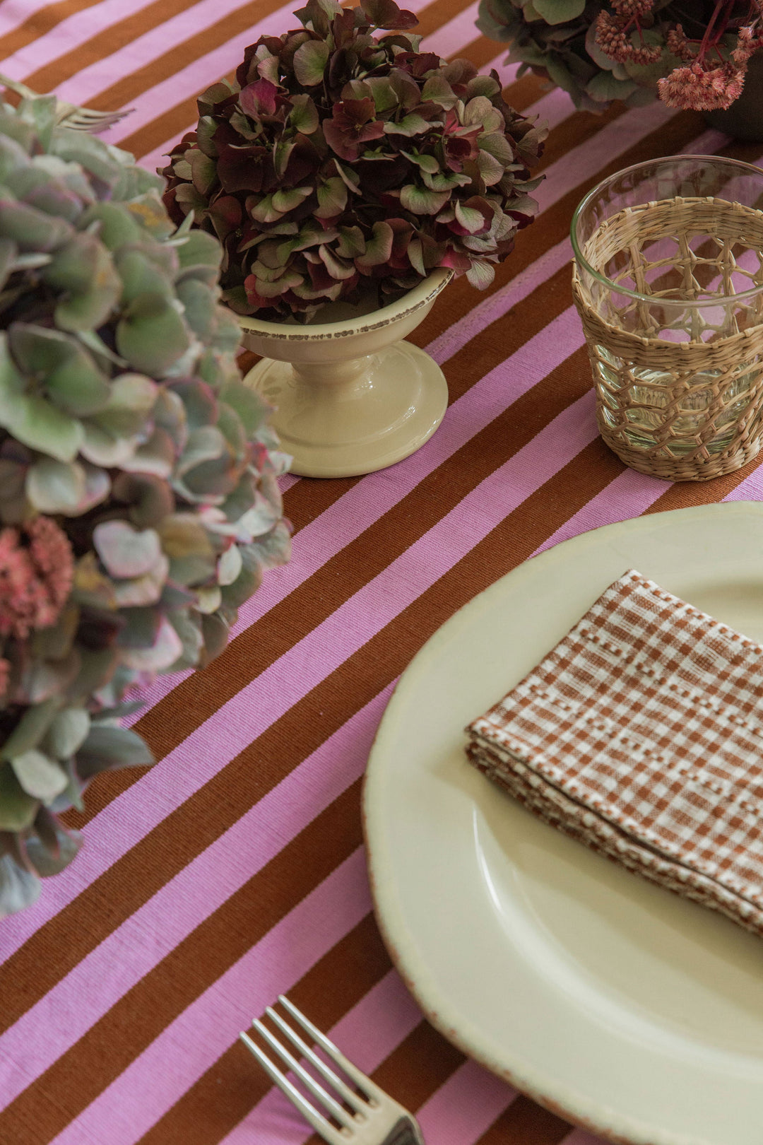 Lilac and nutmeg stripe tablecloth set with a cream plate, cut hydrangea, and a glass tumbler