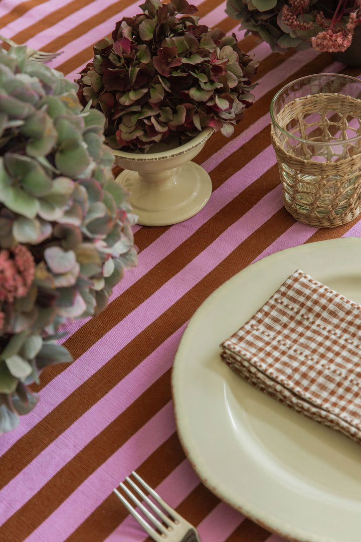 Lilac and nutmeg stripe tablecloth set with a cream plate, cut hydrangea, and a glass tumbler
