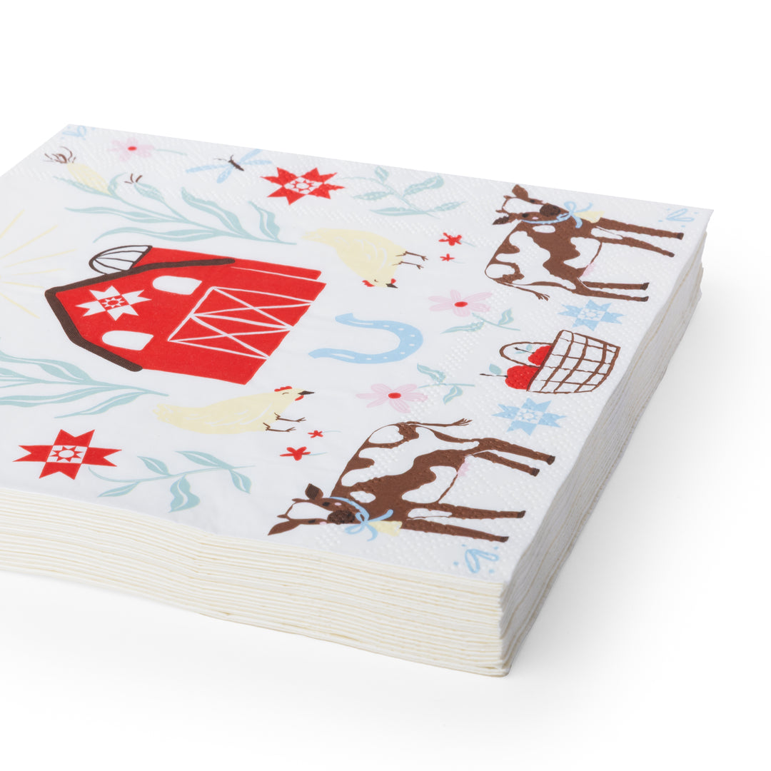 Stack of square white paper napkin featuring a colorful country farm illustration with a red barn, cows, chickens, flowers, and a blue horseshoe.