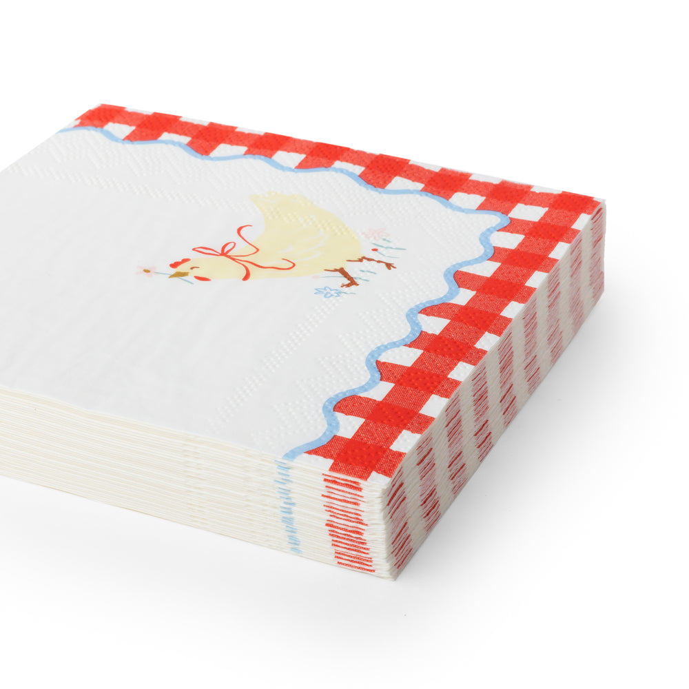 Cocktail white paper napkins featuring a red and white gingham border, a scalloped blue edge, and a small yellow chicken illustration on the top.