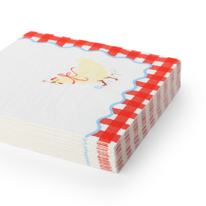 Cocktail white paper napkins featuring a red and white gingham border, a scalloped blue edge, and a small yellow chicken illustration on the top.