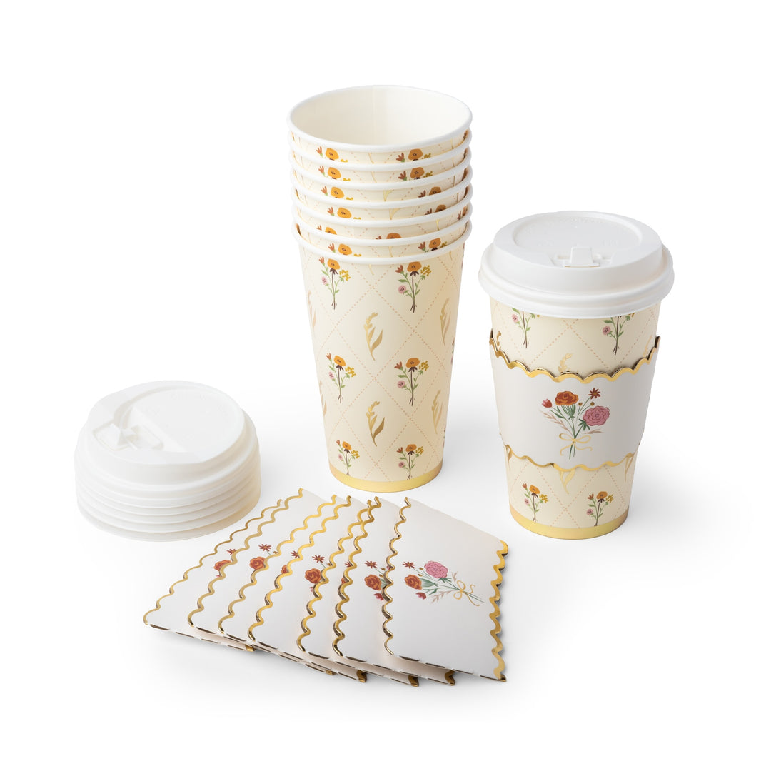 A set of paper disposable cups and napkins with a cream background, gold scalloped borders, and a delicate floral pattern. The set includes a stack of paper cups, a single cup with a white lid and a matching paper sleeve, a stack of white lids, and a stack of folded napkins, all arranged on a clean white background.