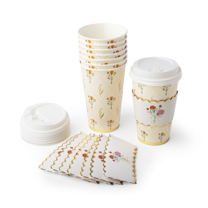 A set of paper disposable cups and napkins with a cream background, gold scalloped borders, and a delicate floral pattern. The set includes a stack of paper cups, a single cup with a white lid and a matching paper sleeve, a stack of white lids, and a stack of folded napkins, all arranged on a clean white background.