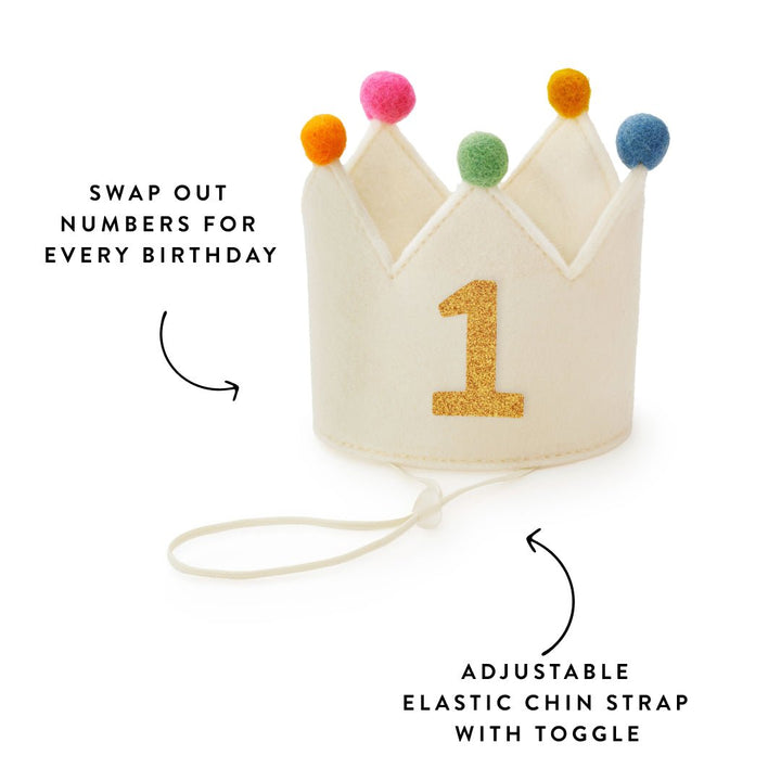 Ivory crown with gold 1 and elastic chin strap, callouts for swappable numbers and the toggle strap