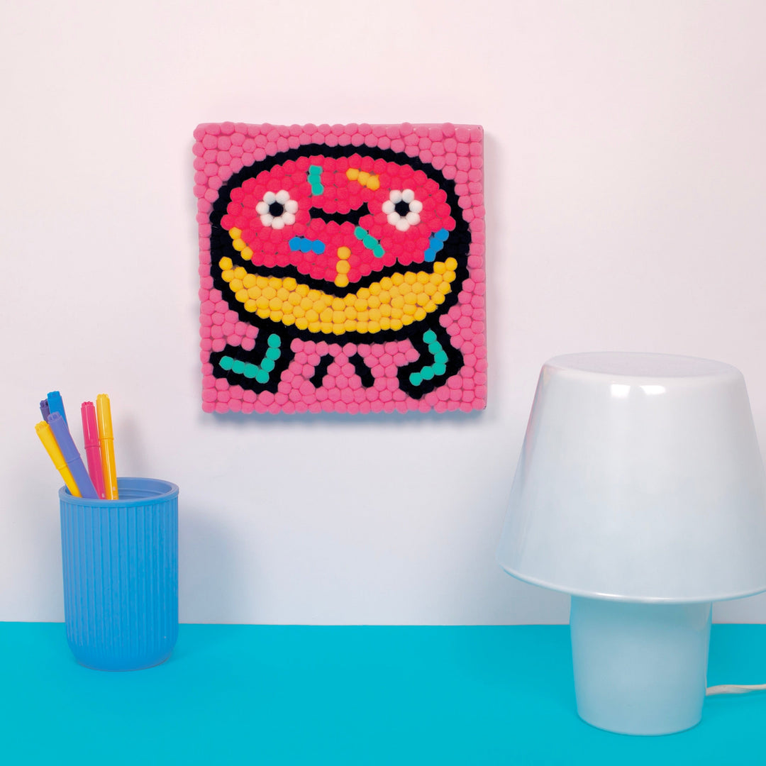 Finished pink donut pom pom artwork displayed on a wall above a table