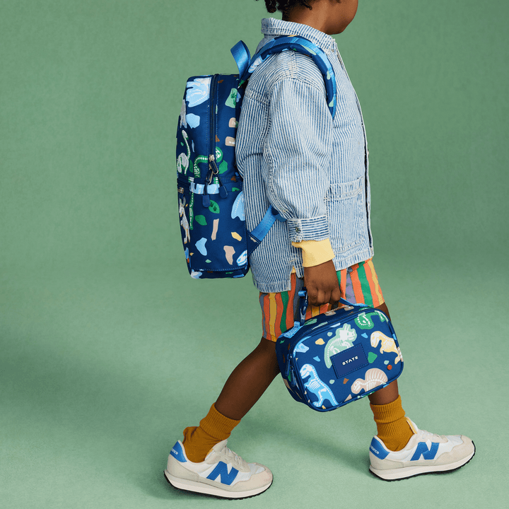 Child in a denim jacket carrying the dinosaur snack bag with a matching Dino Fossils backpack