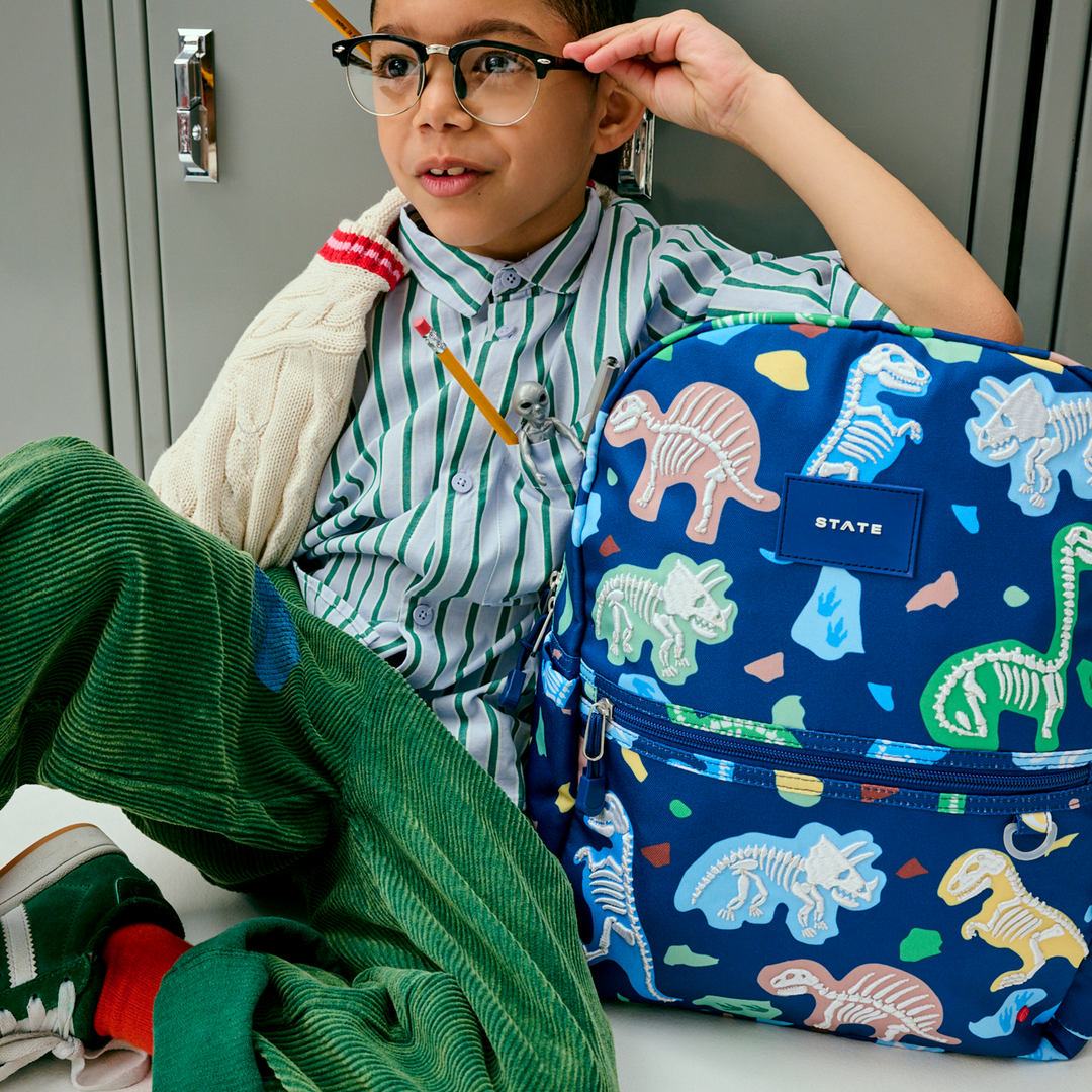 Boy in glasses at school lockers next to the Dino Fossils STATE Kane backpack