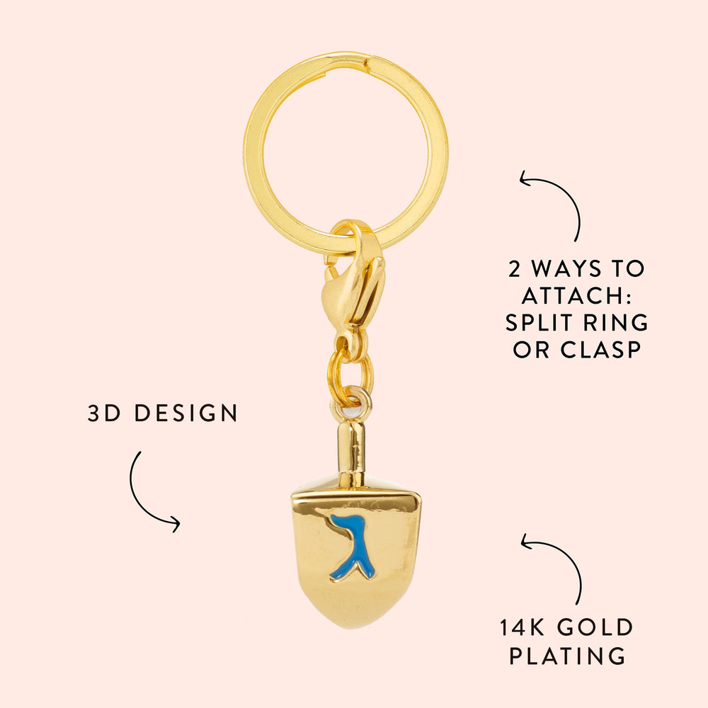 Dreidel charm callout on blush pink noting its 3D design, 14K gold plating, and split ring or clasp attachment