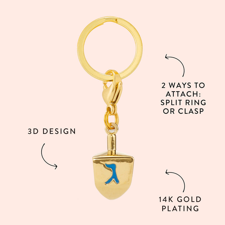 Dreidel charm callout on blush pink noting its 3D design, 14K gold plating, and split ring or clasp attachment