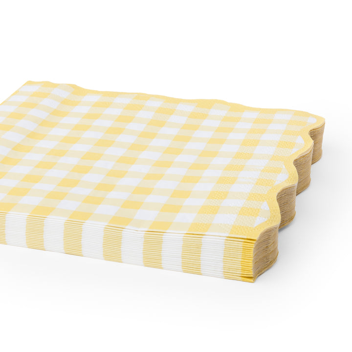 Yellow and white gingham check paper napkins with scalloped edges, shown on a clean white background.A stack of yellow and white gingham check paper napkins with scalloped edges.