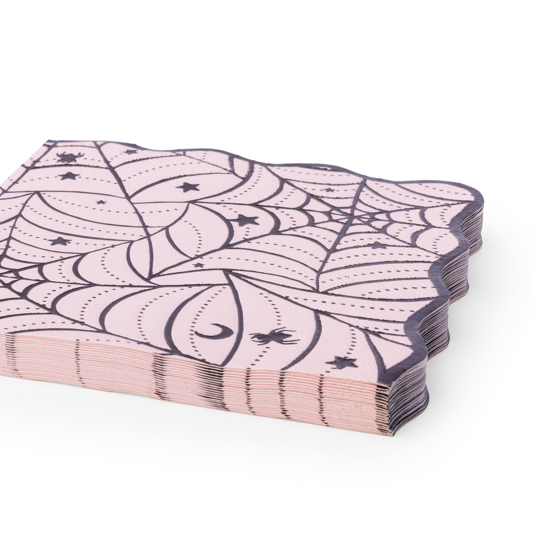 A stack of pink paper napkins with a black spiderweb and moon pattern, shown on a clean white background.