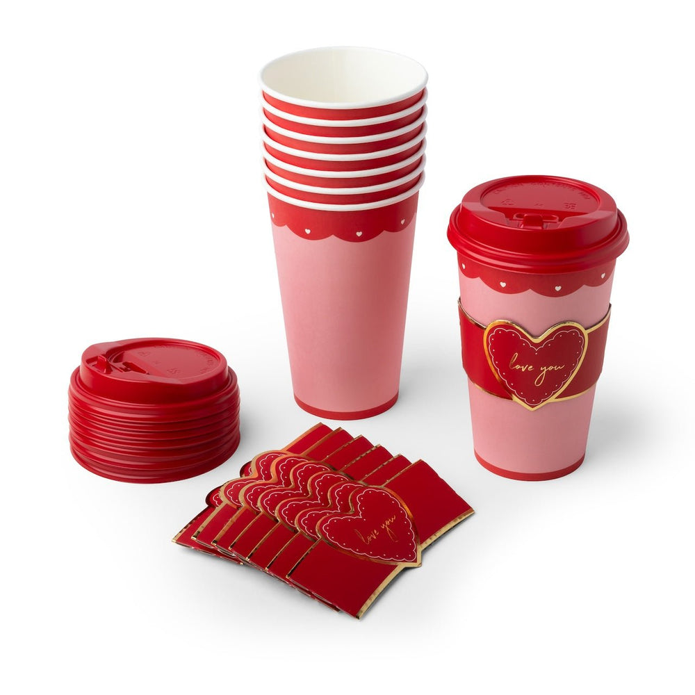 Red and pink Valentine's Day party tableware set including paper cups, a stack of lids, and heart-patterned napkins on a white background.