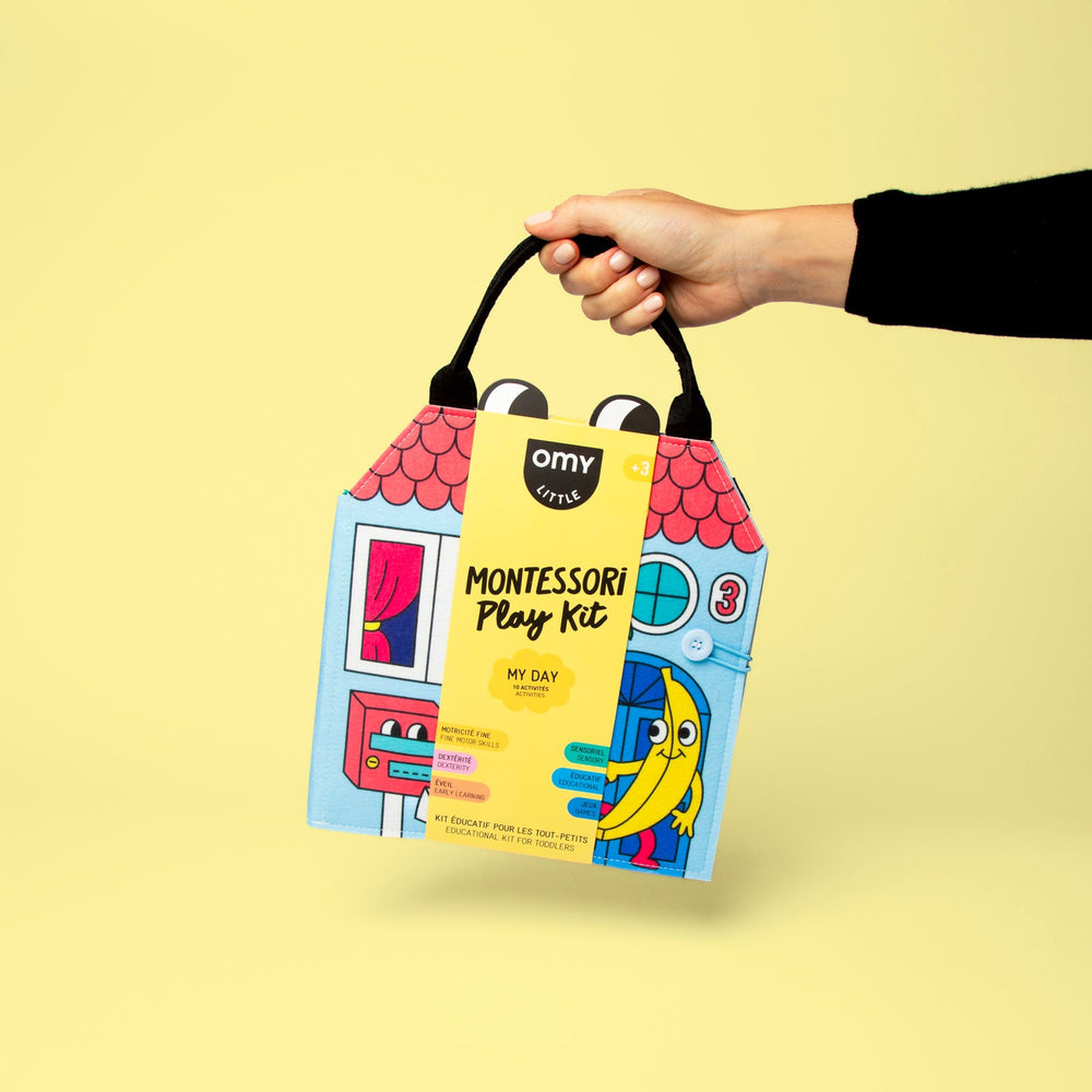 Hand holding the packaged daily-routines Montessori activity kit on a yellow background