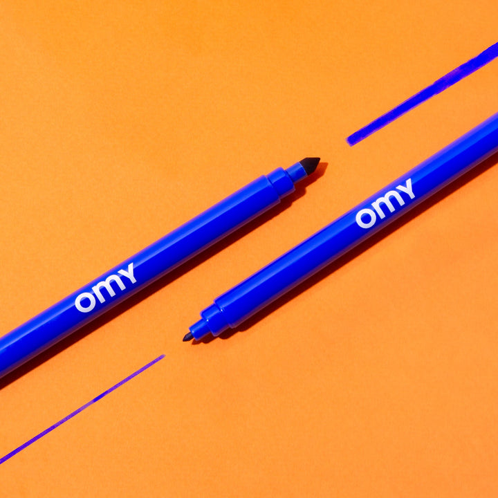 Two double-ended magic markers, one drawing a blue line, on an orange background