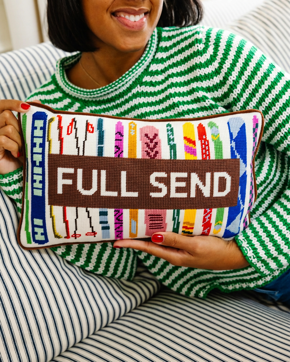 Full Send needlepoint lumbar pillow with colorful ski designs held by a woman in a green striped sweater for a ski or apres ski gift