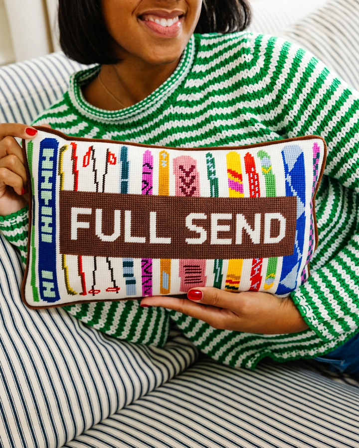 Full Send needlepoint lumbar pillow with colorful ski designs held by a woman in a green striped sweater for a ski or apres ski gift