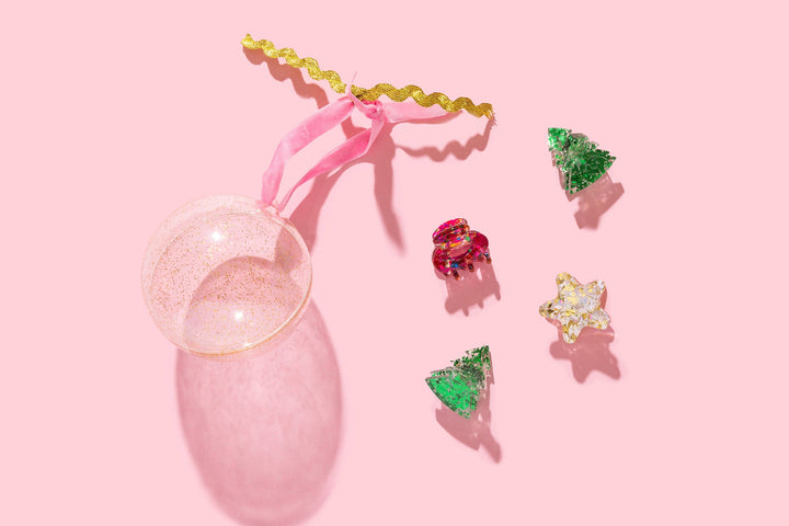 Four mini claw clips shaped as two green trees, a red bow, and a gold star beside an open glitter ball on pink