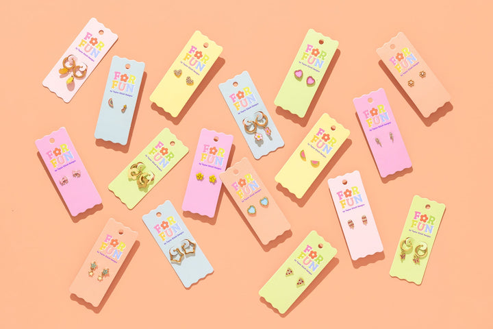 Flat lay of For Fun tween earring cards including pizza slice studs on peach