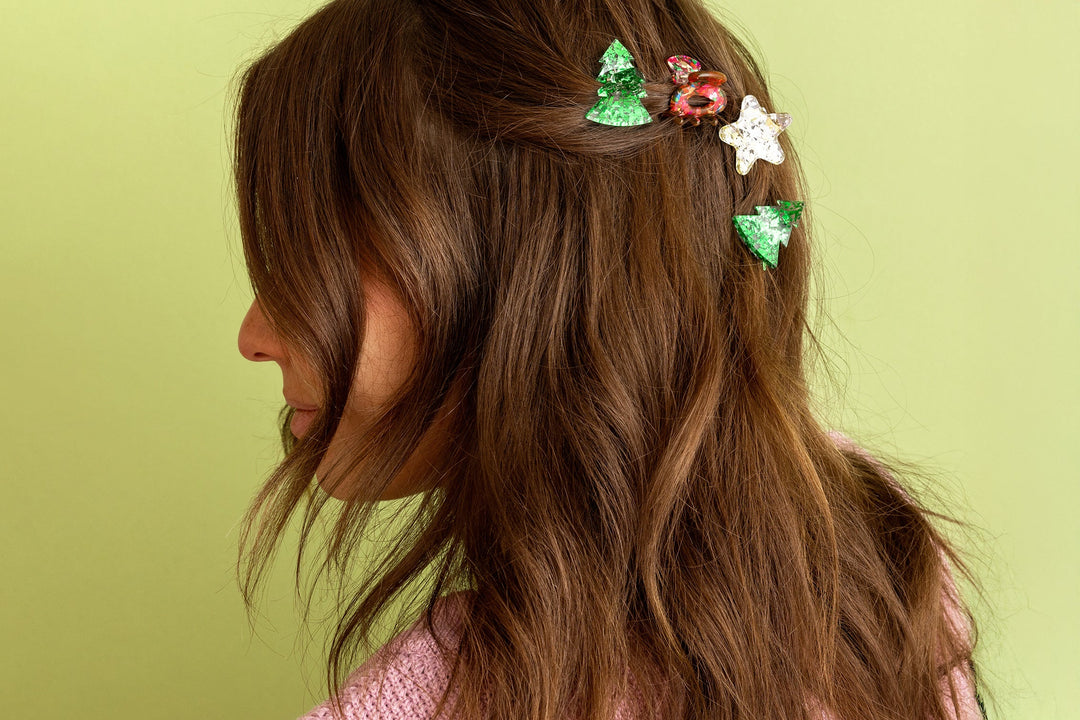 Long brown hair pinned back with green tree, red, and white star claw clips against a green wall
