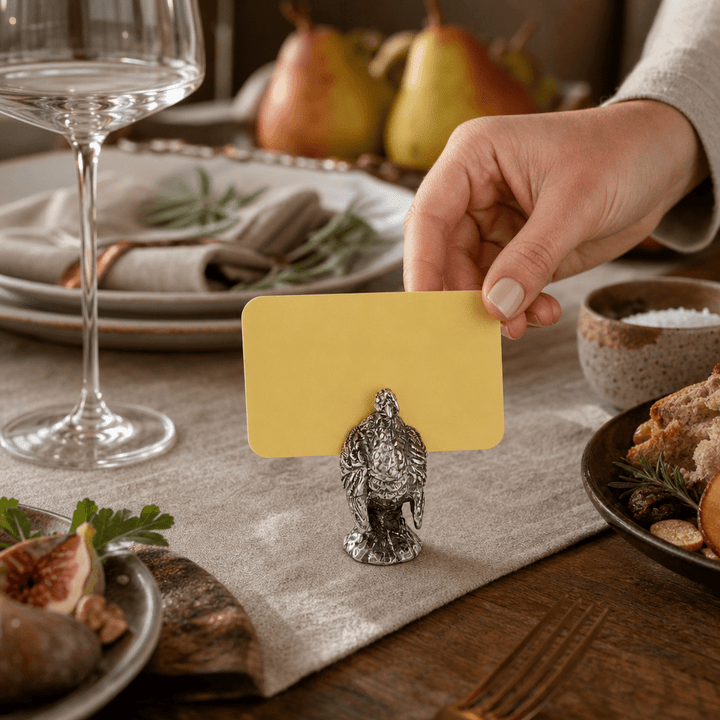 Hand placing a yellow card in a pewter turkey place card holder on a linen table runner