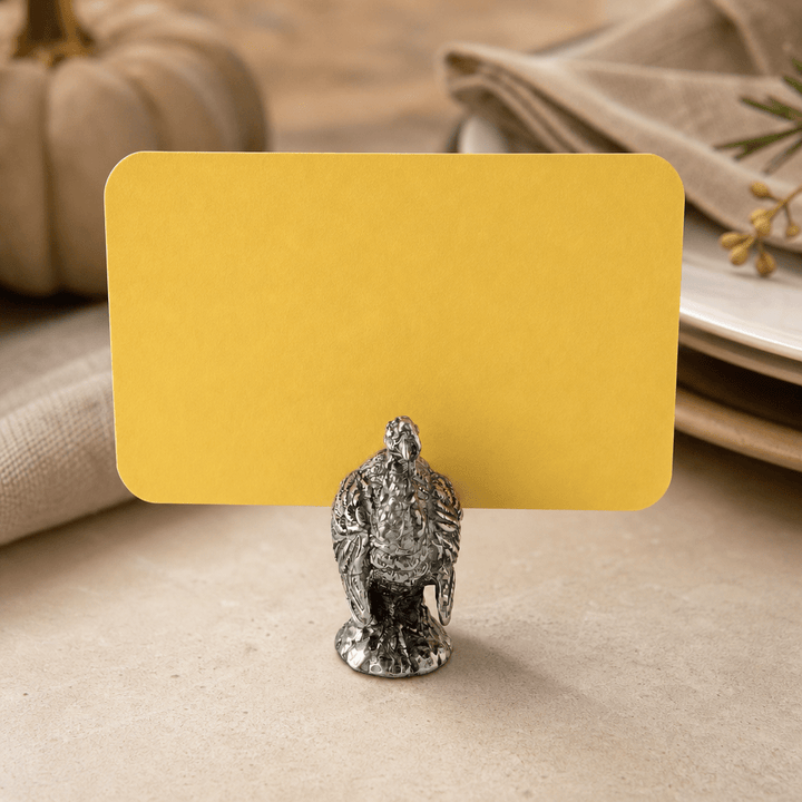 Pewter turkey place card holder with a yellow card on a fall table with white pumpkins
