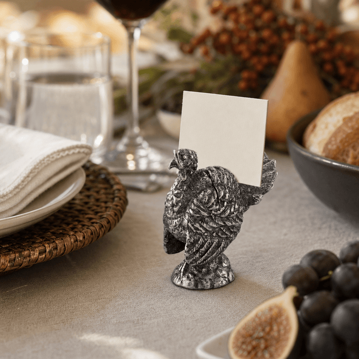 Pewter turkey place card holder with a white card on a harvest table with pears and grapes