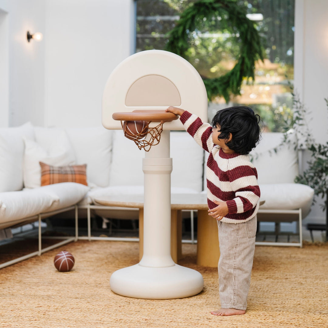 Toddler in a striped sweater dunking at the ivory hoop in a bright living room