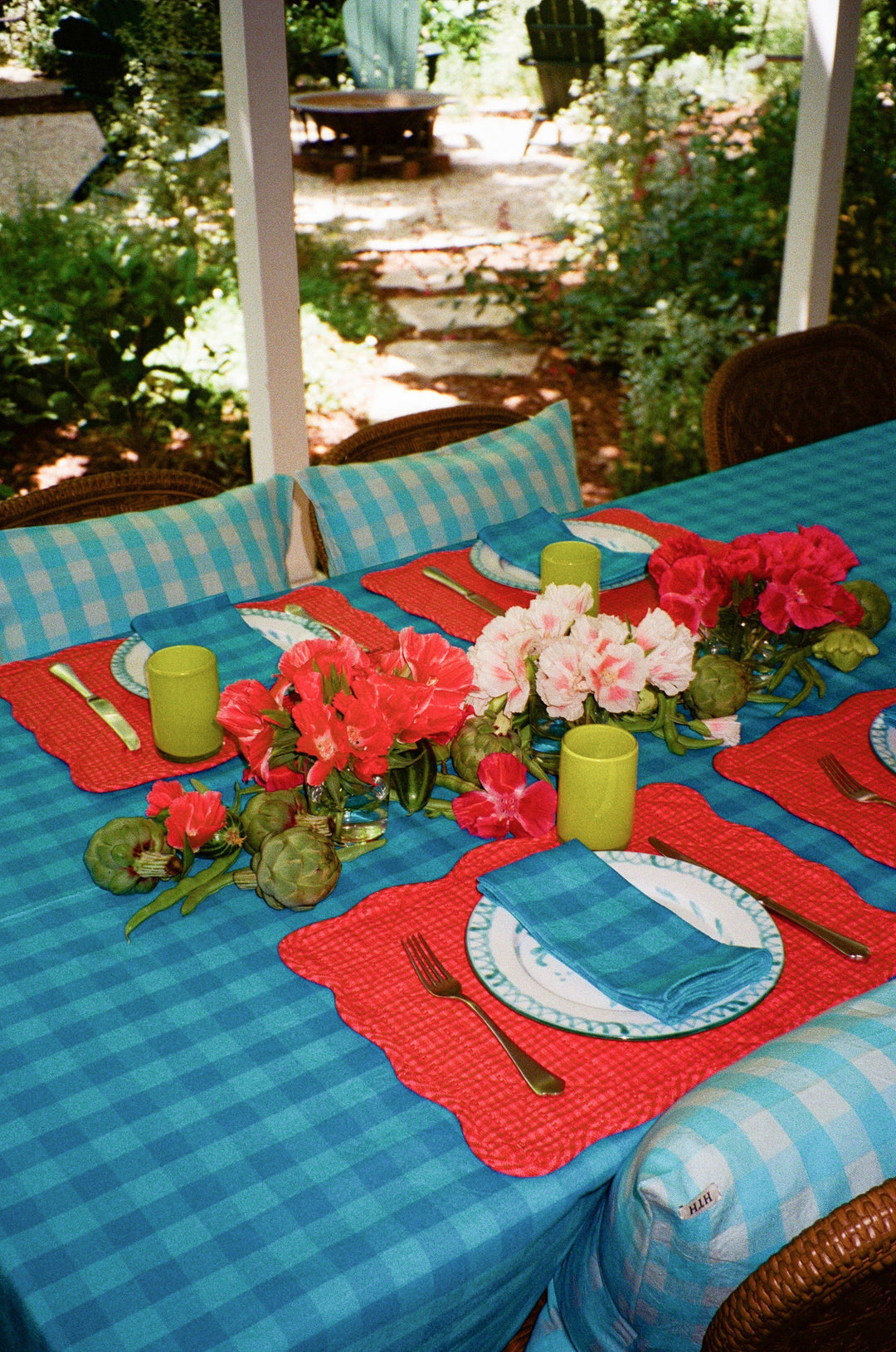 Turquoise gingham napkins on an outdoor summer table with coral placemats and geraniums