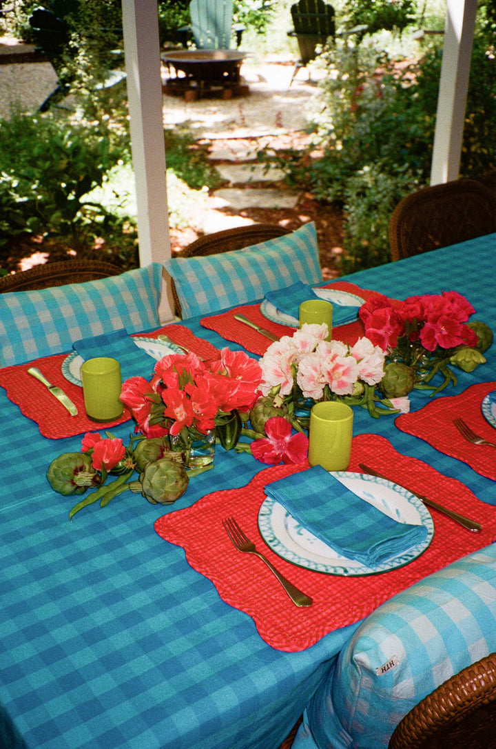 Turquoise gingham napkins on an outdoor summer table with coral placemats and geraniums