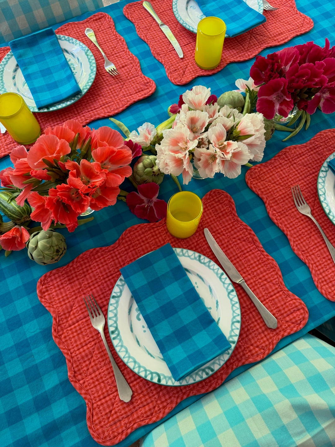 Blue gingham tablecloth on a patio table with coral linens, glassware, and cut flowers