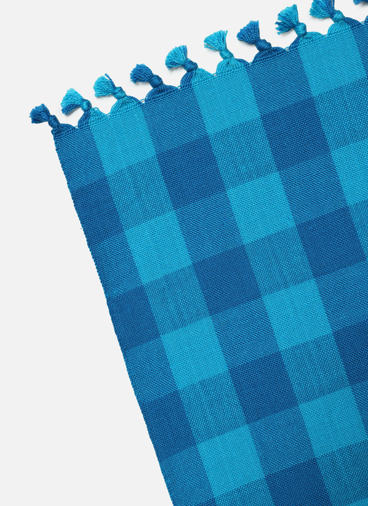 Close-up of the turquoise gingham weave and the knotted tassel edge of the tablecloth