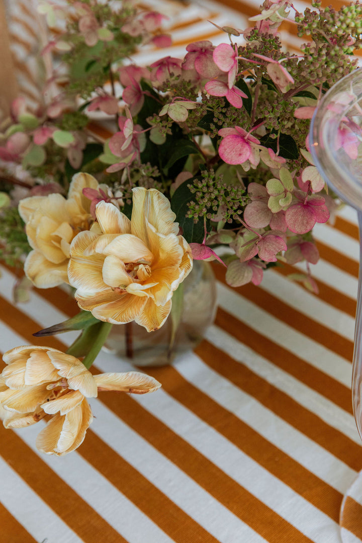Goldenrod stripe tablecloth set with cut roses, hydrangea, and a pillar candle