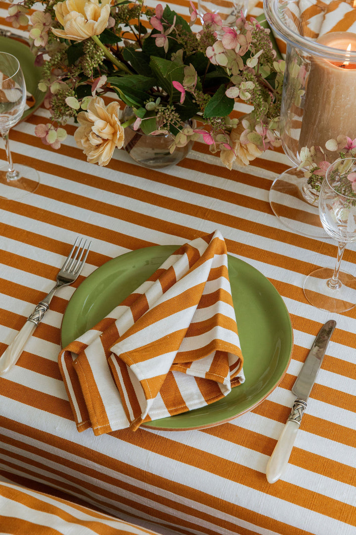 Goldenrod stripe napkin folded on a green plate at a fall place setting with gold flatware