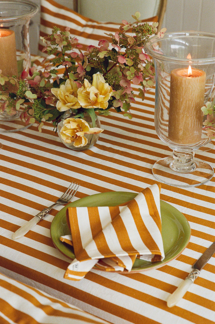 Goldenrod stripe napkin folded on a green plate over the matching stripe tablecloth