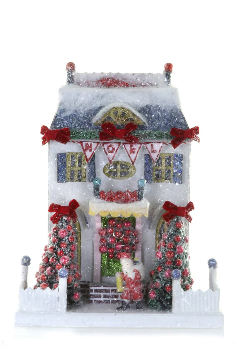 White glitter paper Christmas village house with a Noel banner, Santa, and bottle brush trees for holiday decor