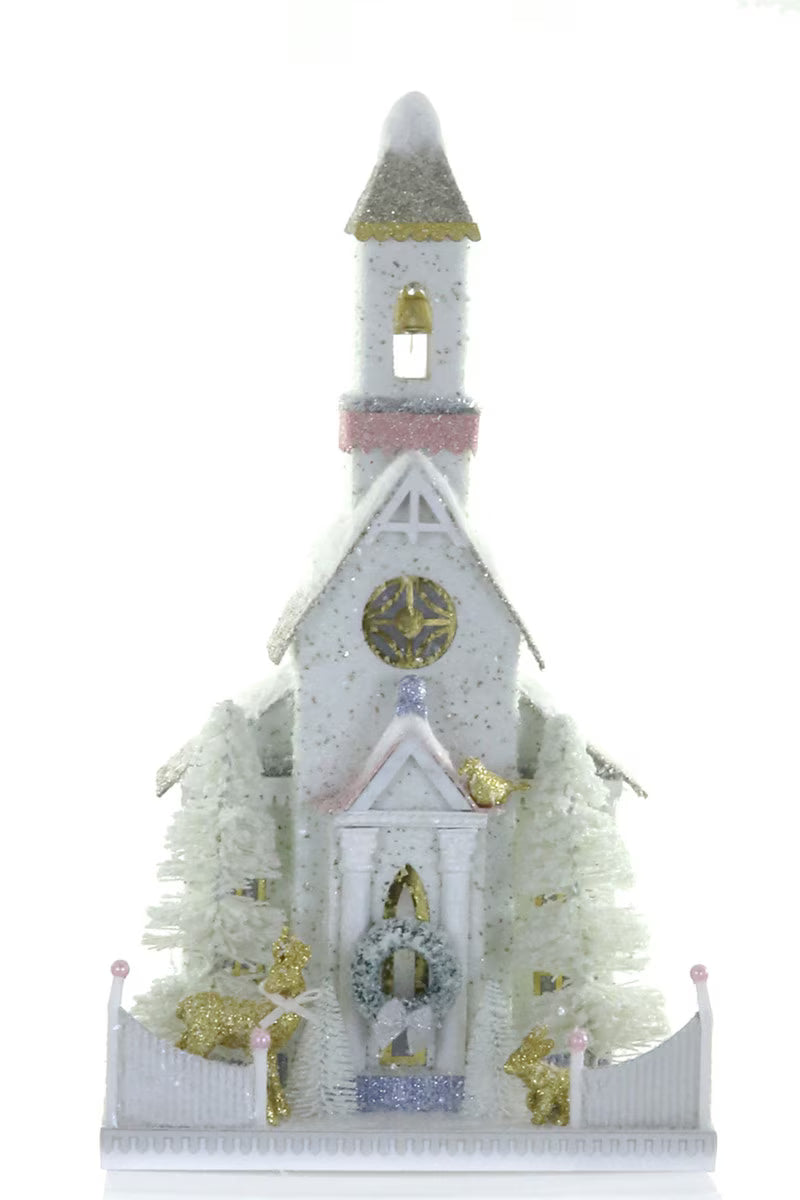 White glitter paper Christmas church with a steeple, bell, gold accents, and bottle brush trees for a holiday village display
