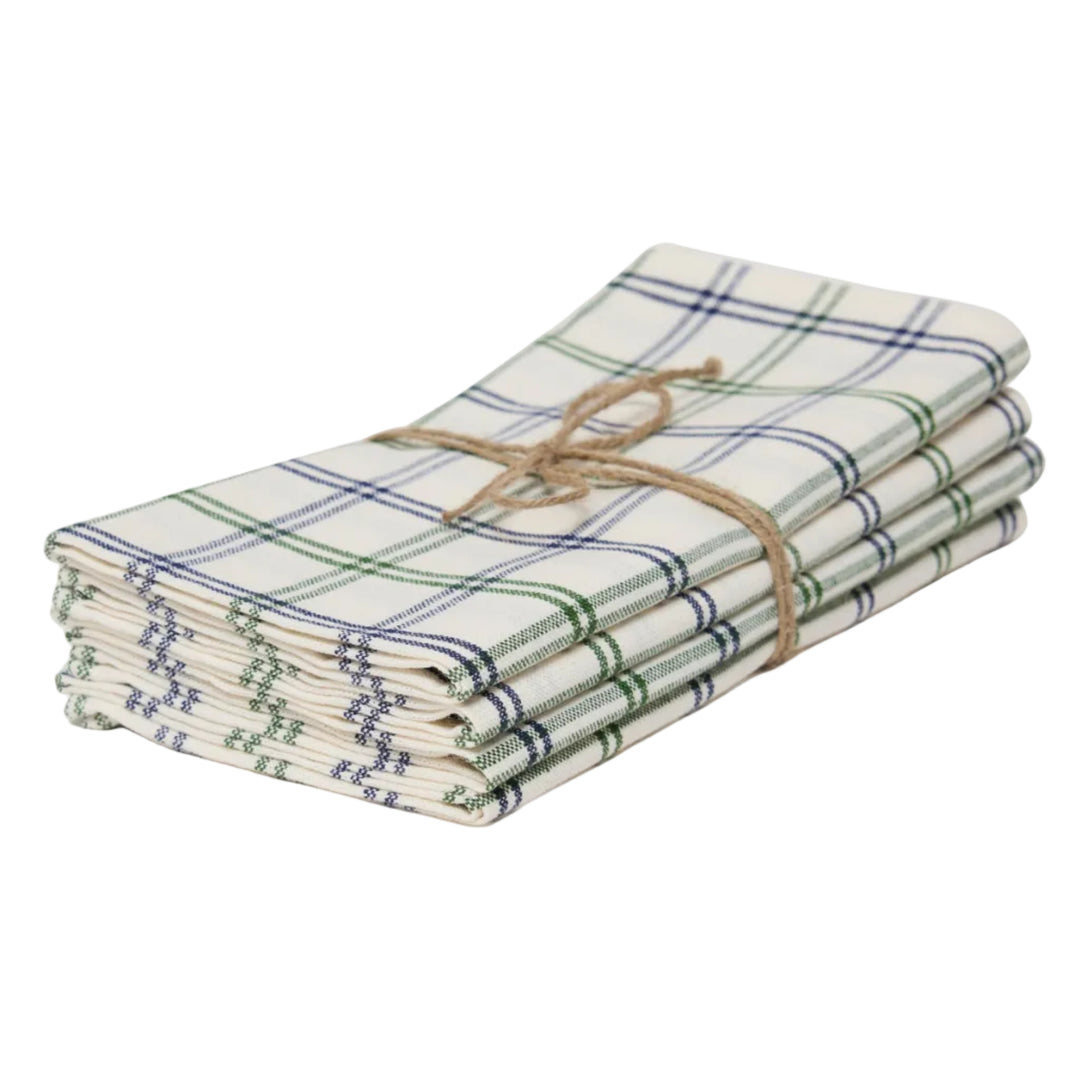 A stack of four folded cotton napkins with a green and blue plaid pattern on a cream background, tied together with a natural jute twine bow, set against a plain light gray background.
