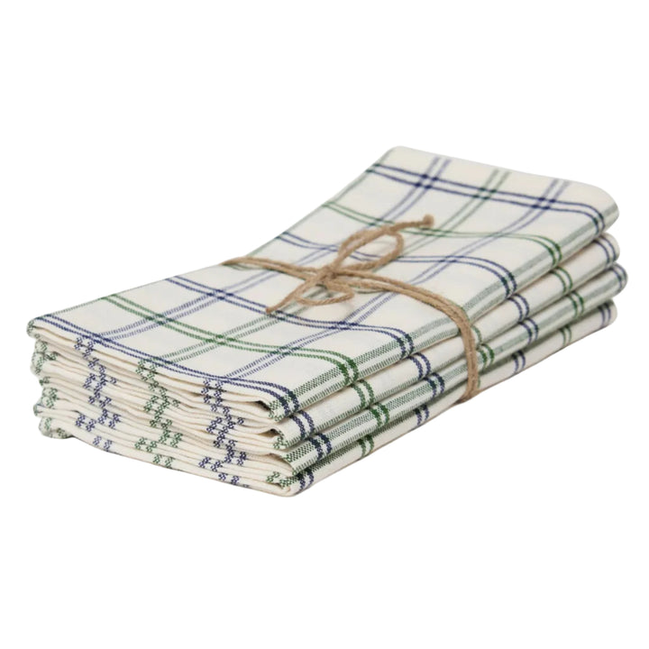 A stack of four folded cotton napkins with a green and blue plaid pattern on a cream background, tied together with a natural jute twine bow, set against a plain light gray background.