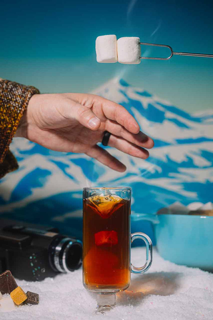 Hand holding a warm s'mores rum toddy in a glass mug by the fire
