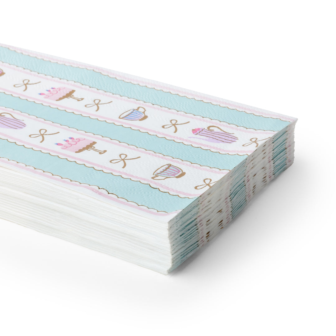 A stack of decorative paper napkins with a pastel pattern of lavender teacups, pink teapots, and gold foil lettering on a light blue and white striped background, shown on a white background.
