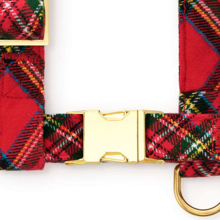 Close-up of the gold side-release buckle, adjustment slider, and D-ring on the red tartan dog harness.