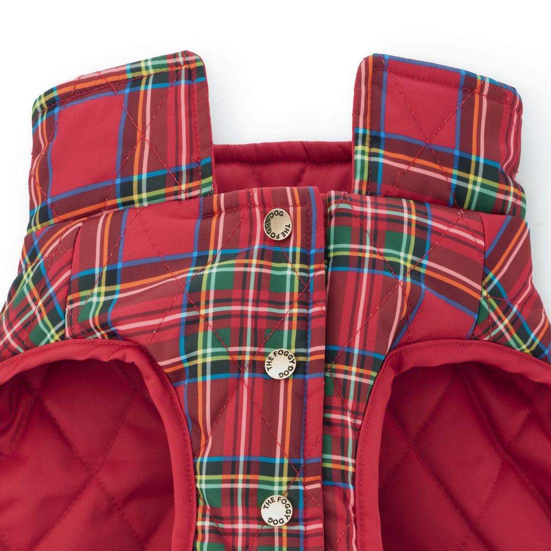 Close-up of a tartan dog jacket's gold snap fasteners, red lining, and quilted plaid fabric.