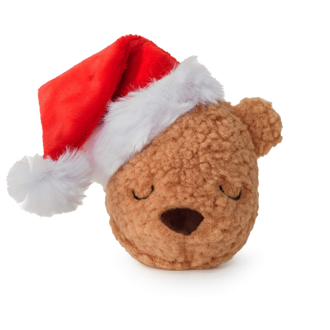 Tan sherpa teddy bear dog toy with sleepy eyes in a red Santa hat on white