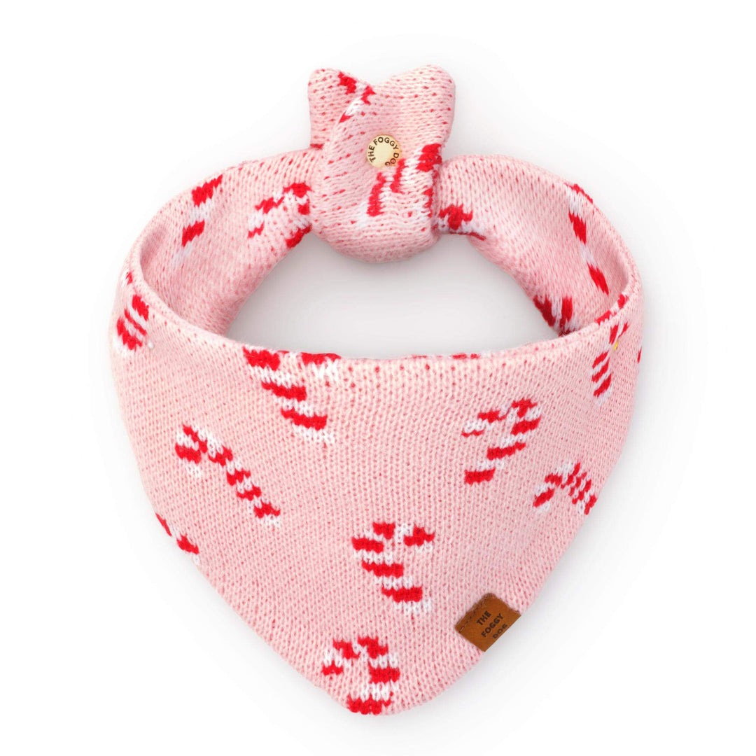 Blush pink knit dog bandana with red and white candy canes, tied in a loop on white