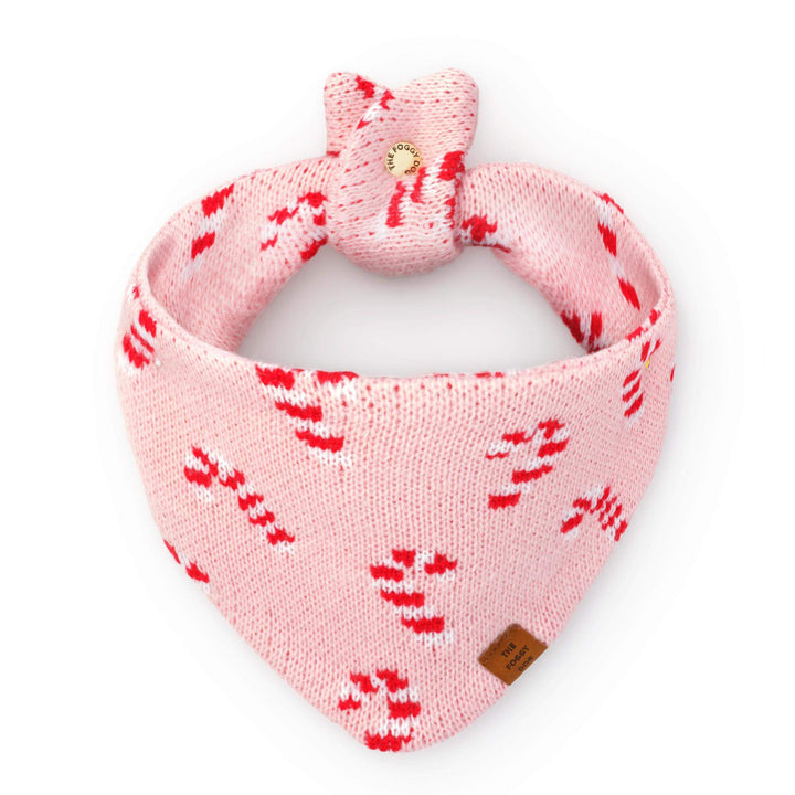 Blush pink knit dog bandana with red and white candy canes, tied in a loop on white