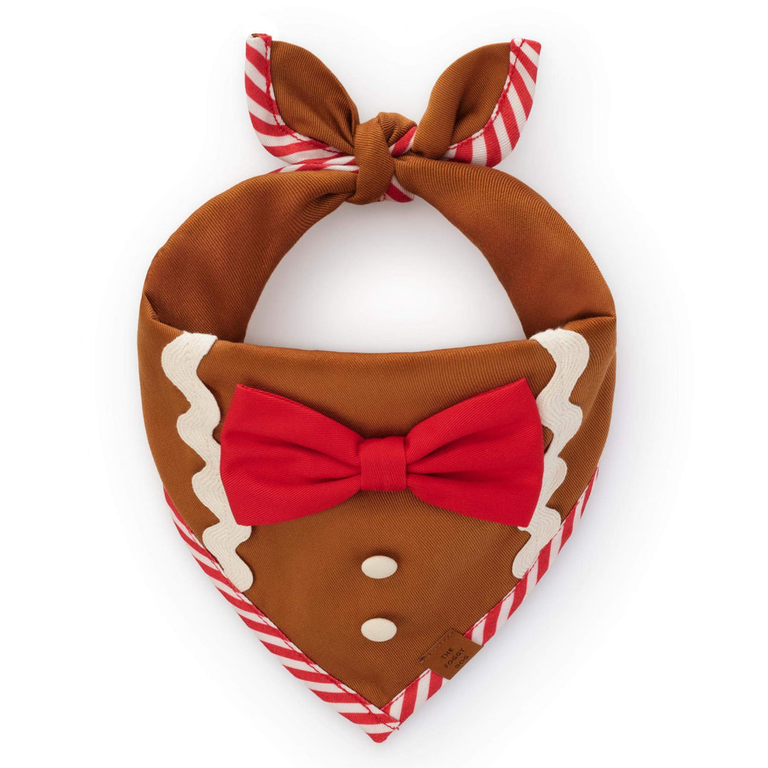 Brown gingerbread-style dog bandana with red bow, two white buttons, white icing trim, and red-and-white striped edging.